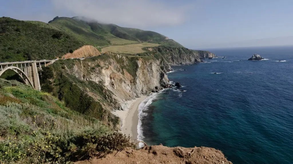 A breathtaking view of a coastal bridge spanning over lush cliffs and azure waters.